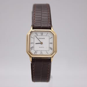 Reloj de cuarzo vintage Tissot 21589 para mujer, caja rectangular dorada, esfera blanca con números romanos, correa de cuero marrón.