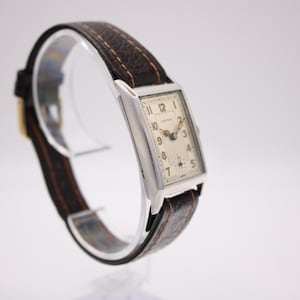 Left-side view of the PRONTO watch highlighting the rectangular case profile and brown strap on a stand.