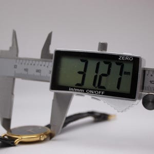 Digital caliper measuring the watch case, with the display clearly showing '31.27 mm'.