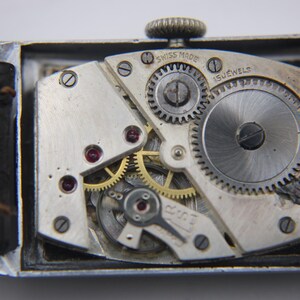 Macro shot of the "SWISS MADE 15 JEWELS" manual wind movement, showing gears and ruby jewels inside the open case.