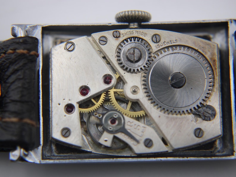Macro shot of the "SWISS MADE 15 JEWELS" manual wind movement, showing gears and ruby jewels inside the open case.
