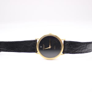 Full frontal view of the Raymond Weil watch unbuckled, lying flat, showcasing the gold case, black dial, and black leather strap.