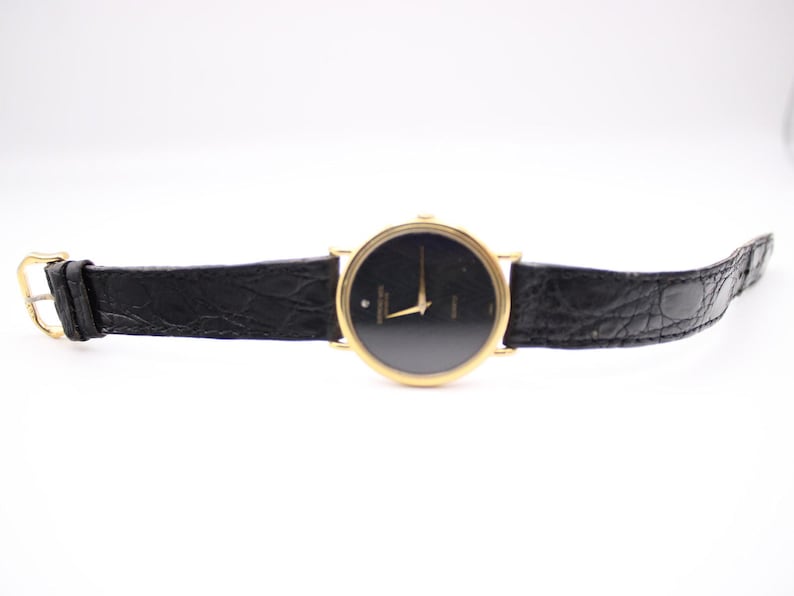 Full frontal view of the Raymond Weil watch unbuckled, lying flat, showcasing the gold case, black dial, and black leather strap.