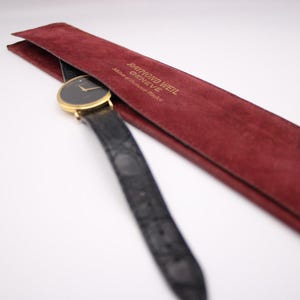 The Raymond Weil watch with its black strap partially placed inside its original red velvet pouch.