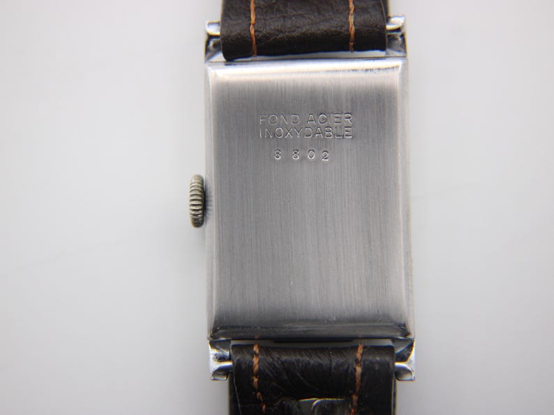 Close-up of the polished stainless steel case back with "FOND ACIER INOXYDABLE" and serial number 3802 engraving.
