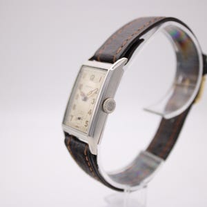 Right-side view of the PRONTO watch showing the crown, rectangular silver case, and strap.