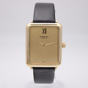 May include: A gold-toned rectangular wristwatch with a black leather band. The watch face features Roman numerals and the brand name "RAYMOND WEIL GENEVE". The watch has a gold-colored bezel and a crown on the right side.