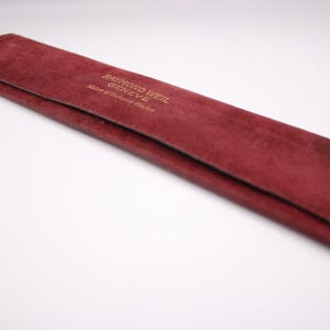 Close-up of the red velvet Raymond Weil Genève pouch, featuring the gold embossed brand logo and text.