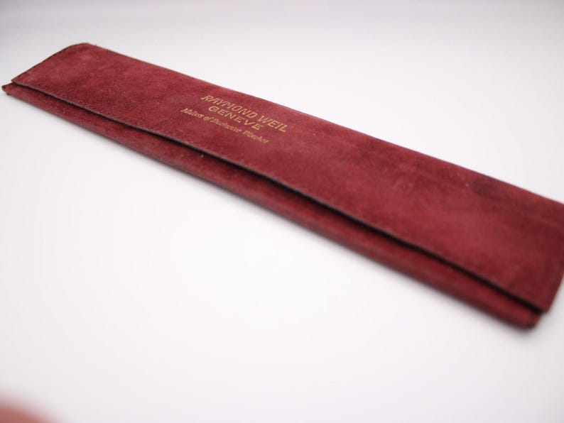 Close-up of the red velvet Raymond Weil Genève pouch, featuring the gold embossed brand logo and text.