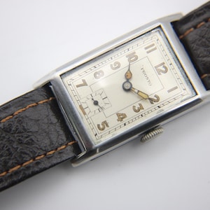 Angled close-up of the PRONTO watch dial, showcasing the cream face, legible Arabic numerals, and small seconds sub-dial.