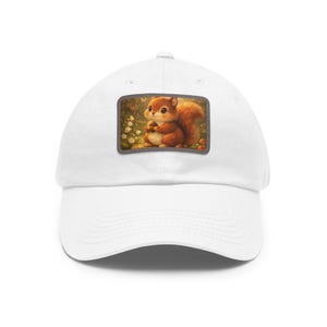 May include: A white baseball cap featuring a rectangular patch on the front. The patch displays a detailed illustration of a small, brown, fluffy squirrel holding a nut, set against a soft, warm-toned background with white flowers and greenery.