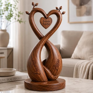 May include: A dark brown wooden sculpture featuring two intertwined forms that create a heart shape. A small heart-shaped pendant hangs in the centre with the text Forever Together. The names Emma and Liam are engraved on the base structures.