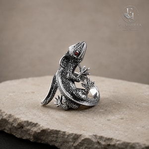 Handcrafted-style sterling silver lizard ring featuring intricate texture, wrap design, and red eye details. Distinctive reptile jewelry that combines artistic craftsmanship with a bold statement look.