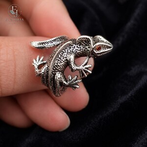 Close-up of a sterling silver gecko ring showcasing intricate scales, sculptural craftsmanship, and vibrant red eye accents. Unique animal jewelry designed for those who appreciate detailed reptile-inspired accessories.