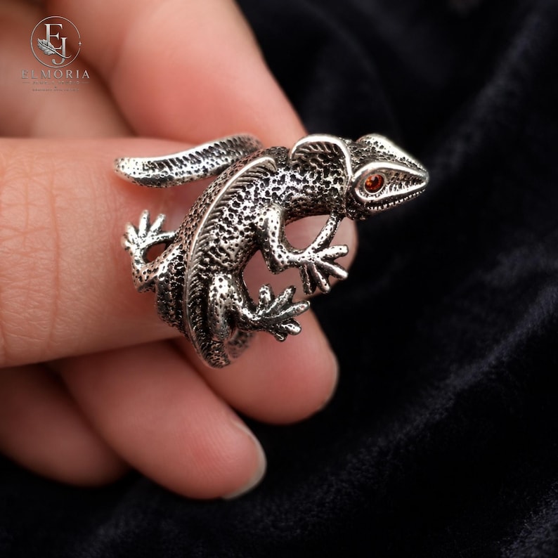 Close-up of a sterling silver gecko ring showcasing intricate scales, sculptural craftsmanship, and vibrant red eye accents. Unique animal jewelry designed for those who appreciate detailed reptile-inspired accessories.