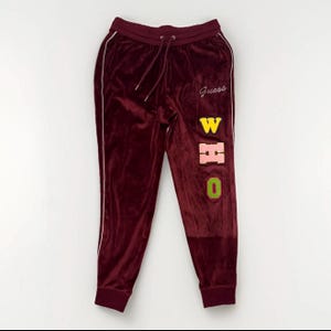 May include: Burgundy velour sweatpants with white side stripes and a drawstring waist. The word "Guess" is embroidered in white, and the letters "WHO" are appliqued in yellow, pink, and green.