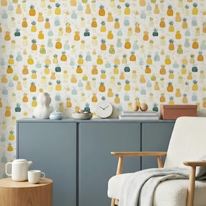 Könnte beinhalten: Ein Raum mit einem blauen Schrank, einem weißen Stuhl und einem hölzernen Beistelltisch. Die Tapete ist mit einem sich wiederholenden Muster aus gelben, grünen und blauen Ananas bedeckt. Eine weiße Teekanne und Tasse stehen auf dem Tisch. Eine weiße Uhr und Dekorationsartikel befinden sich auf dem Schrank.