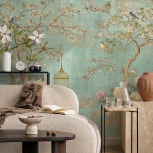 Może przedstawiać: Spokojna scena we wnętrzu z jasną sofą, ciemnym drewnianym stolikiem kawowym i dekoracyjnym muralem z motywem kwiatowym i ptasim w odcieniach zieleni, złota i różu. Akcesoria: wazon, zegar i dekoracyjna klatka dla ptaków.