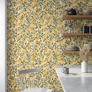 May include: A kitchen with lemon-patterned wallpaper, featuring yellow lemons and green leaves on a cream backdrop. Wooden shelves display crockery and a teapot. A white chair and marble countertop are in the foreground.