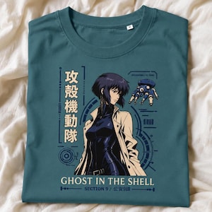 Può includere: Una t-shirt a maniche corte color verde acqua con la grafica di un personaggio dai capelli scuri in trench, un piccolo carro armato robotico blu, testo giapponese e la scritta inglese Ghost in the Shell Section 9, con linee tecniche circolari.