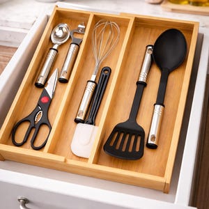 Może przedstawiać: Drewniany organizer do szuflady wypełniony przyborami kuchennymi. Zawiera łyżkę, otwieracz do butelek, trzepaczkę, szpatułkę, łopatkę szczelinową i nożyczki. Przybory mają srebrne uchwyty i czarne lub białe końc&oacute;wki robocze. Szuflada jest biała.