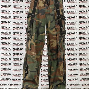 May include: Camouflage cargo pants with black straps, buckles, and silver hardware. The pants have multiple pockets and a drawstring waist. The brand name "NEXARO APPAREL" is printed on the background.