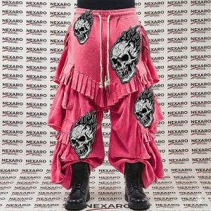 May include: Pink, layered pants with a drawstring waist and black boots. The pants feature multiple skull patches with flames. The background is covered in a repeating pattern of the word "NEXARO APPAREL".