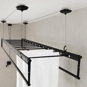 Könnte beinhalten: Ein schwarzer, an der Decke montierter Wäschetrockner mit mehreren horizontalen Stangen. Der Trockner wird von Kabeln getragen, die an Deckenrollen befestigt sind. Weißer Stoff hängt daran. Für den Innenbereich konzipiert.