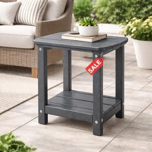 May include: A dark gray outdoor side table with a lower shelf. A small white pot with a green plant and a book rest on top. A red "SALE" tag hangs from the side. The table is made of a durable material and is designed for outdoor use.