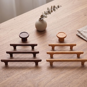 May include: A collection of wooden cabinet hardware including two round knobs and six bar-style pulls. The set features dark brown wood and light tan wood finishes, each with a smooth, rounded design and two mounting points for installation.