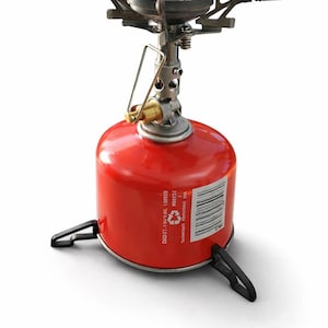 Op de afbeelding: Een compacte, rode campingbrander met een zilveren brander en zwarte steunen. De brander heeft een cilindrische brandstoftank en opvouwbare armen. Ideaal voor buiten koken en backpacken.