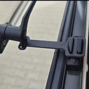 Puede incluir: Un pestillo de ventana de plástico negro con un diseño rectangular. El pestillo está fijado a un marco de ventana y a un cristal. El pestillo tiene una palanca y un mecanismo de bloqueo. El pestillo de la ventana está diseñado para asegurar una ventana.