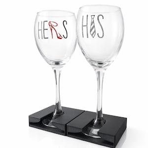 Può includere: Due calici trasparenti con le parole "HERS" e "HIS". Il calice "HERS" ha un tacco rosso, e il calice "HIS" ha una cravatta. Sono posti in un supporto nero.