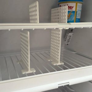 May include: White refrigerator interior with wire shelves and white plastic dividers. A container of butter is visible on the top shelf. The dividers are perforated with small holes.