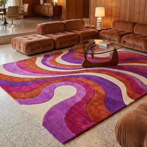 Könnte beinhalten: Ein lebendiger Teppich im Retro-Stil mit einem wirbelnden Muster in Lila-, Orange- und Cremetönen. Der Teppich befindet sich in einem Wohnzimmer mit braunen Samtsofas und einem Glastisch, was eine warme, einladende Atmosphäre schafft.