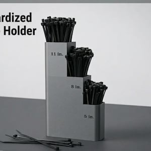 May include: A gray, tiered, standardized zip tie holder containing black zip ties. The three levels are labeled 11 in., 8 in., and 5 in. to organize different lengths. Several loose black zip ties are positioned in front of the holder.