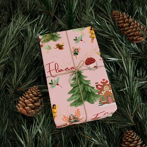 May include: A wrapped gift with a pink background, decorated with illustrations of fairies, mushrooms, and a gingerbread house. The gift is tied with twine and the name "Fliana" is written on the wrapping paper.