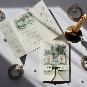 Puede incluir: Juego de papelería de boda con ilustraciones de acuarela de un edificio y un paisaje. La invitación incluye los nombres "Sarah y Robert" y la fecha "07 de agosto". También hay hilo decorativo, perlas y un candelabro dorado.
