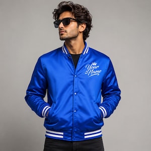 Male model wearing royal blue satin varsity bomber jacket with custom embroidered chest logo design.