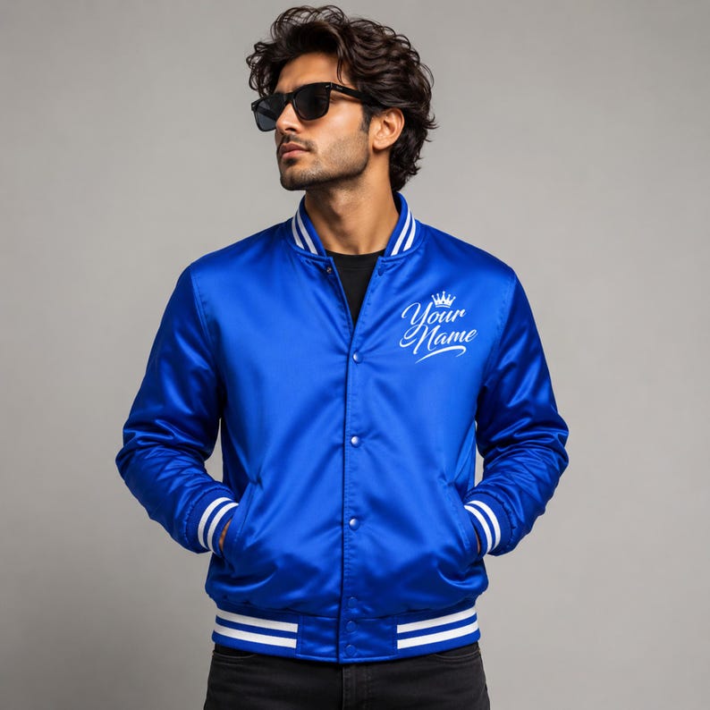 Male model wearing royal blue satin varsity bomber jacket with custom embroidered chest logo design.