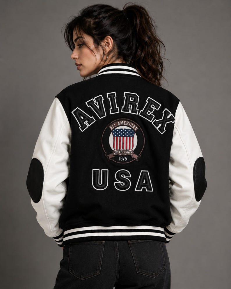 Female model wearing black and white varsity jacket back view with oversized embroidered AVIREX logo