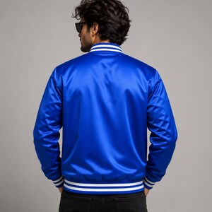 Rear back view of glossy royal blue satin varsity jacket worn by fashionable male model.
