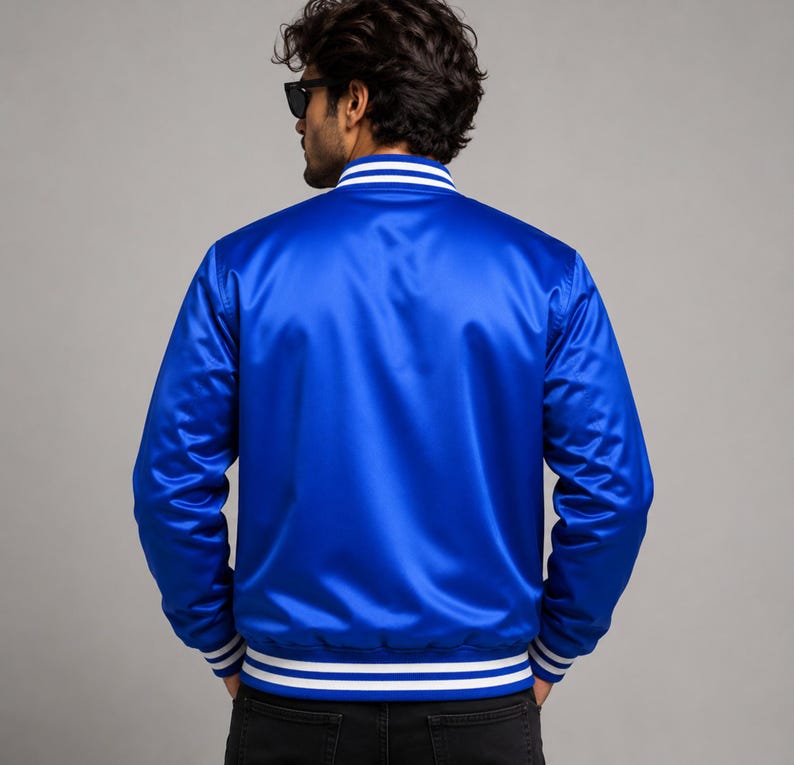Rear back view of glossy royal blue satin varsity jacket worn by fashionable male model.