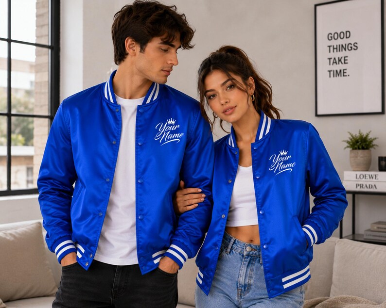 Matching couple wearing royal blue satin varsity bomber jackets in modern indoor streetwear lifestyle setting.