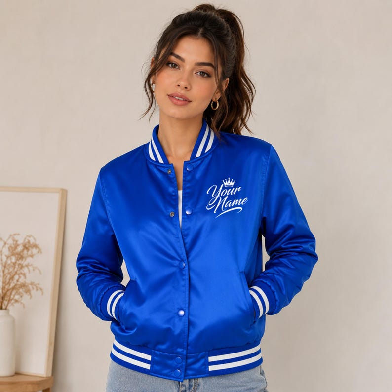 Female model posing in royal blue satin varsity bomber jacket with personalized embroidered branding detail.