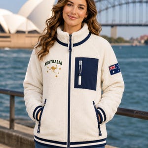 Women's Australia Sherpa Fleece Jacket in cream teddy fleece with navy chest pocket, navy rib trim, Australian flag sleeve patch, kangaroo embroidery and Sydney Opera House waterfront background.