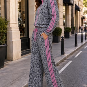 Puede incluir: Un conjunto de dos piezas a juego compuesto por una chaqueta de manga larga con cremallera y pantalones de pierna ancha. Las prendas presentan un estampado de leopardo gris con rayas verticales de color rosa brillante en mangas y piernas.