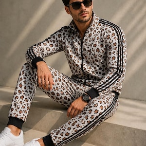 Puede incluir: Un conjunto de chándal a juego con estampado de leopardo en tonos marrón, negro y crema. La chaqueta tiene una cremallera frontal completa, cuello alto y rayas negras en las mangas. El pantalón tiene puños negros y rayas a juego.