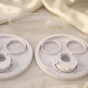 Peut inclure: Deux couvercles circulaires en plastique blanc avec des centres filet&eacute;s et deux petites ouvertures circulaires, pr&eacute;sentant un texte en relief indiquant MODEL P, PATENT PENDING, SEAL et FEED, avec un flacon souple transparent.