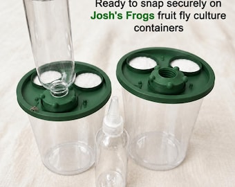 May include: Two clear plastic containers with dark green lids, each featuring two white circular inserts and a central threaded opening. One container has a clear bottle attached. Text reads: Ready to snap securely on Josh's Frogs fruit fly culture containers.